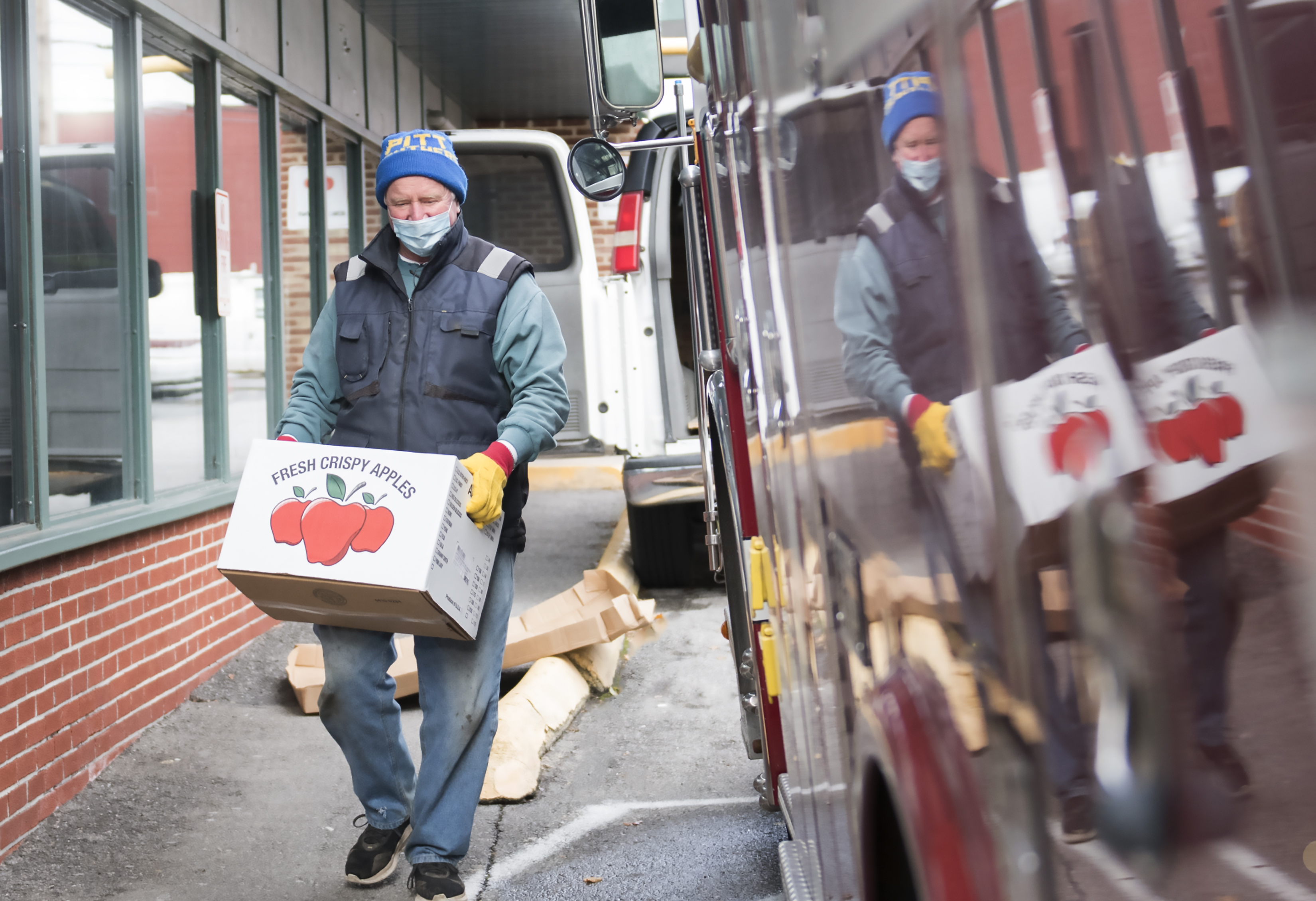 Jim Yonushonis, a volunteer with the YMCA of Centre County, carries a box of fresh apples to distribute for free to local families outside the YMCA in Bellefonte.