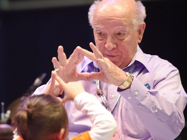 Charles Millard and a child look at each other and make diamond symbol with their hands.