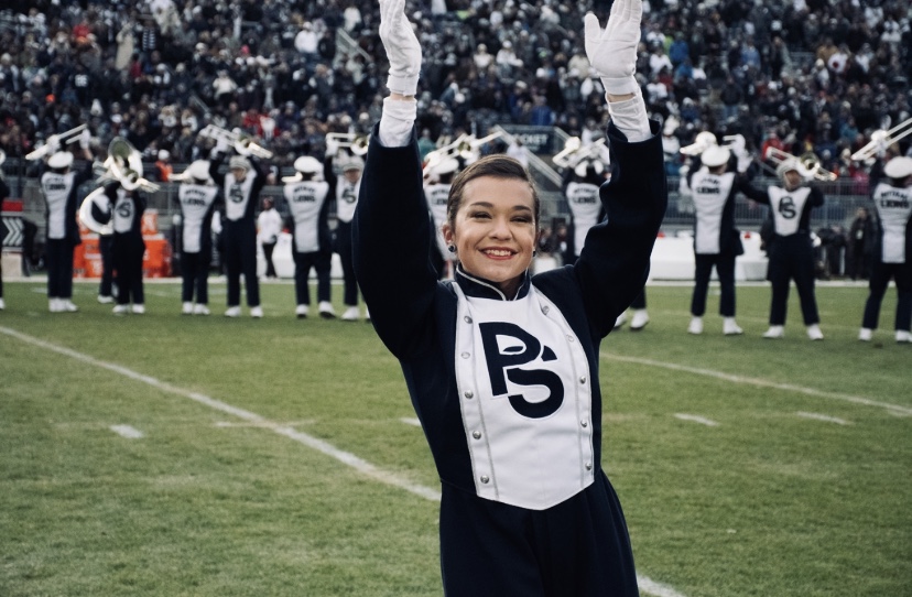 Jenna Fitzpatrick, in a Blue Band uniform with arms raised, leads her squad during a halftime show at Beaver Stadium