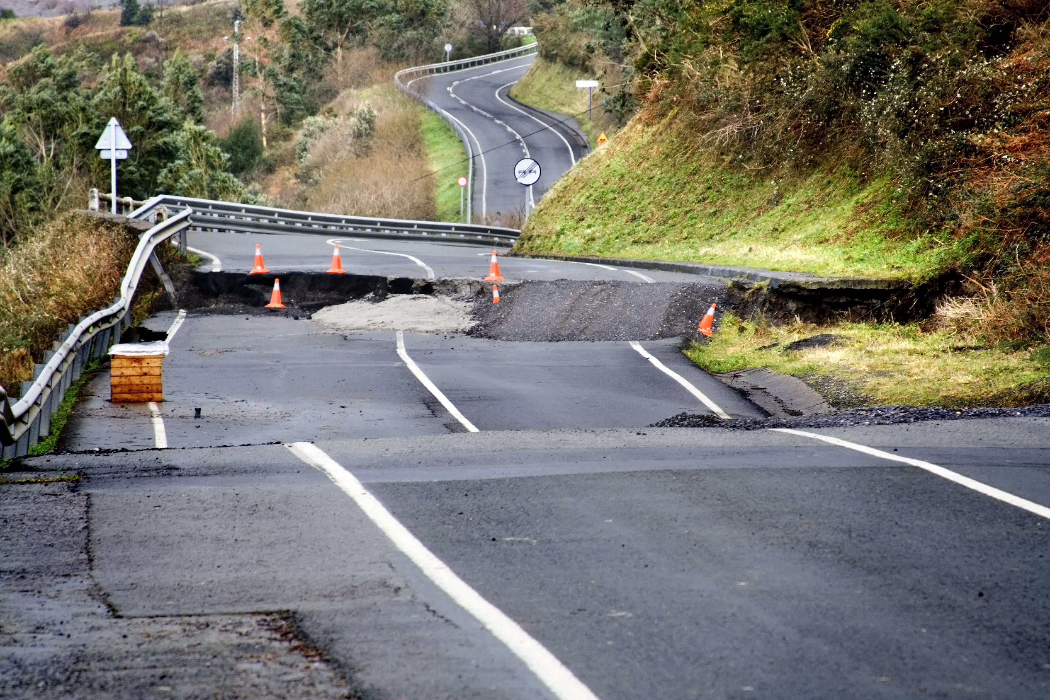 A damaged road shows sections that are cracked and missing.