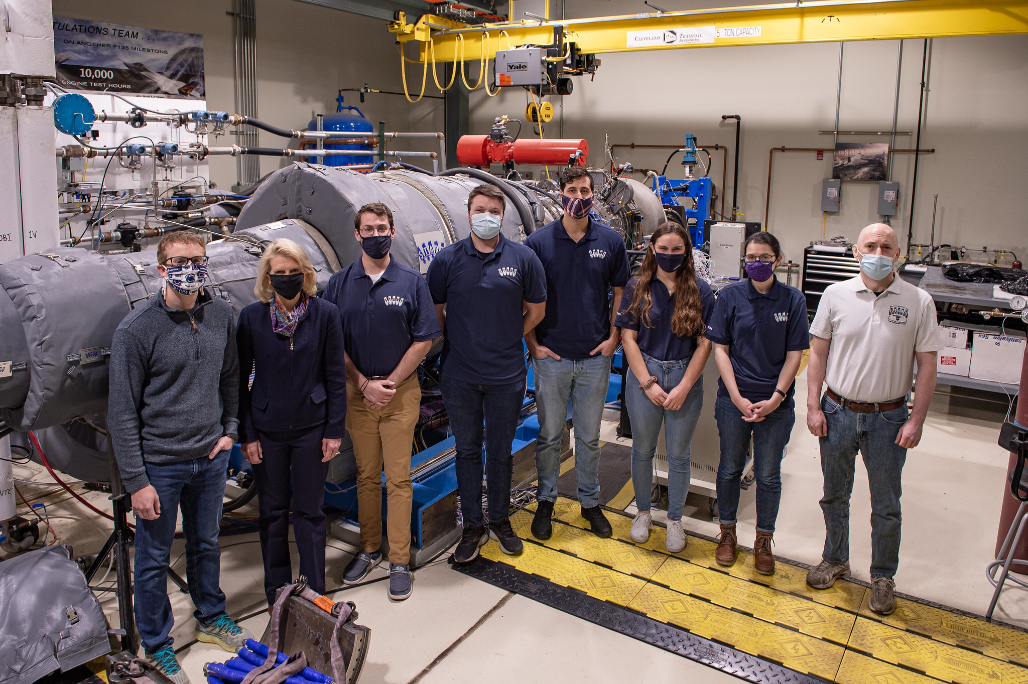 A team of researchers working on sustainable aircraft pose in front of a gas turbine engine. 