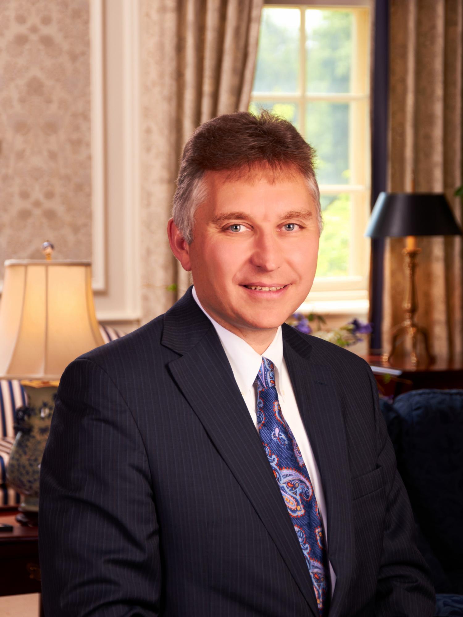 A man in a suit smiles for his headshot image.