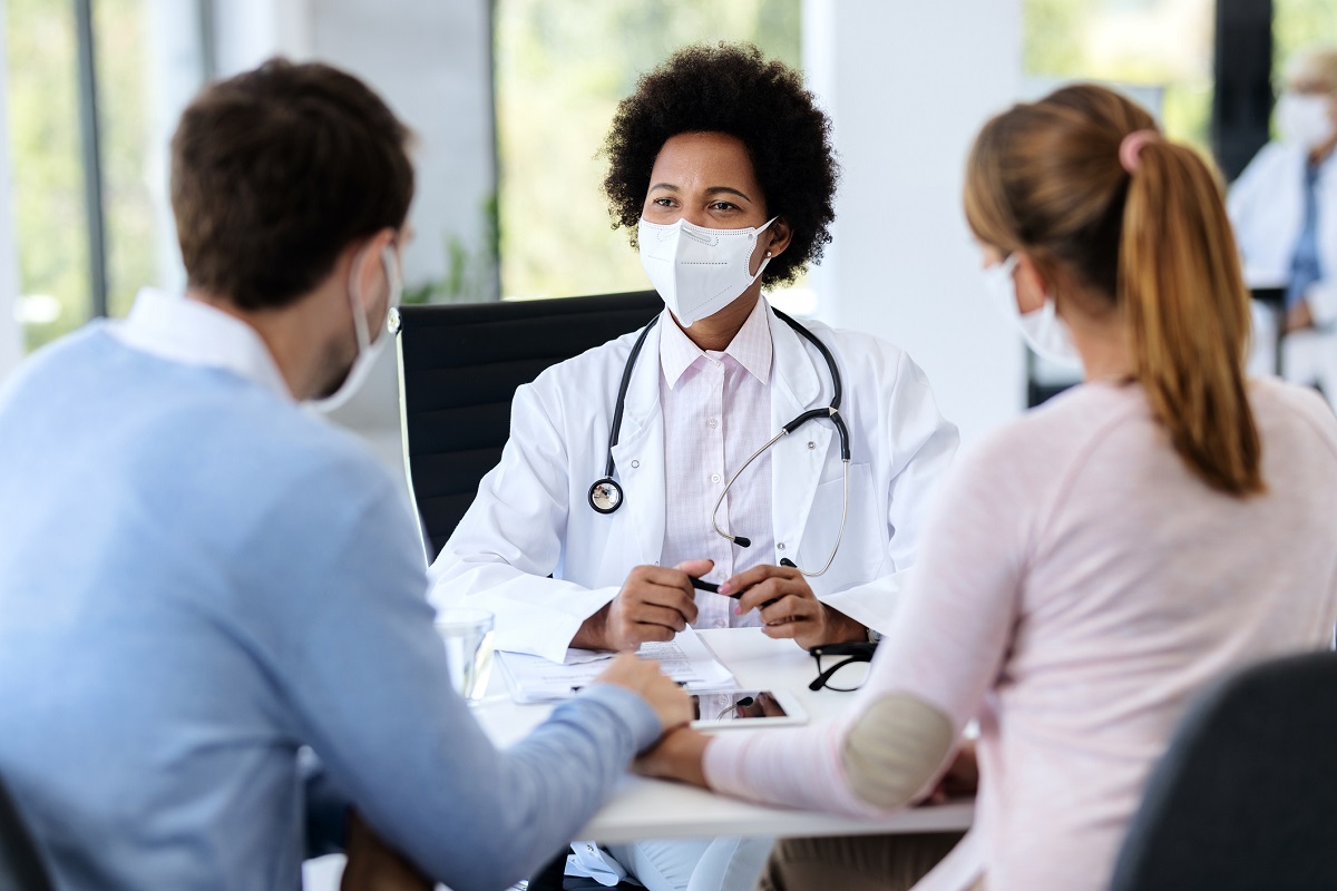 A doctor wearing protective face mask meets with a couple at a clinic.