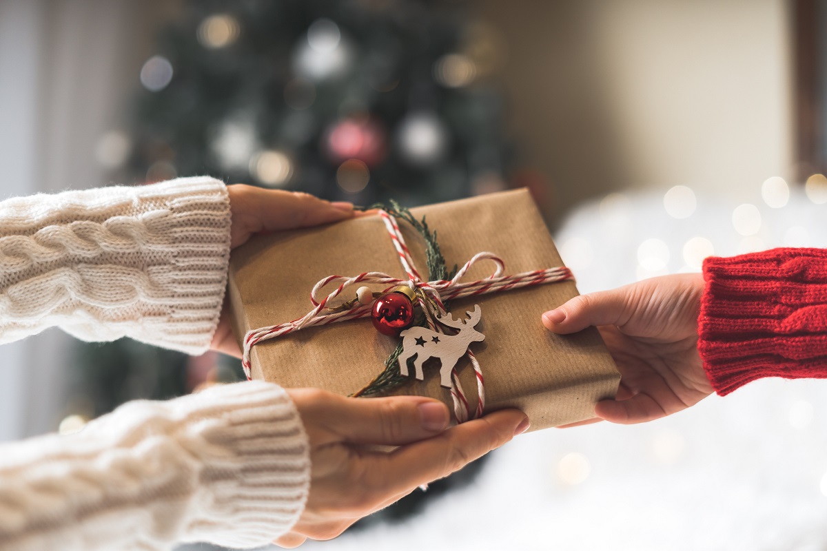 Woman in sweater giving a wrapped Christmas gift box to child.