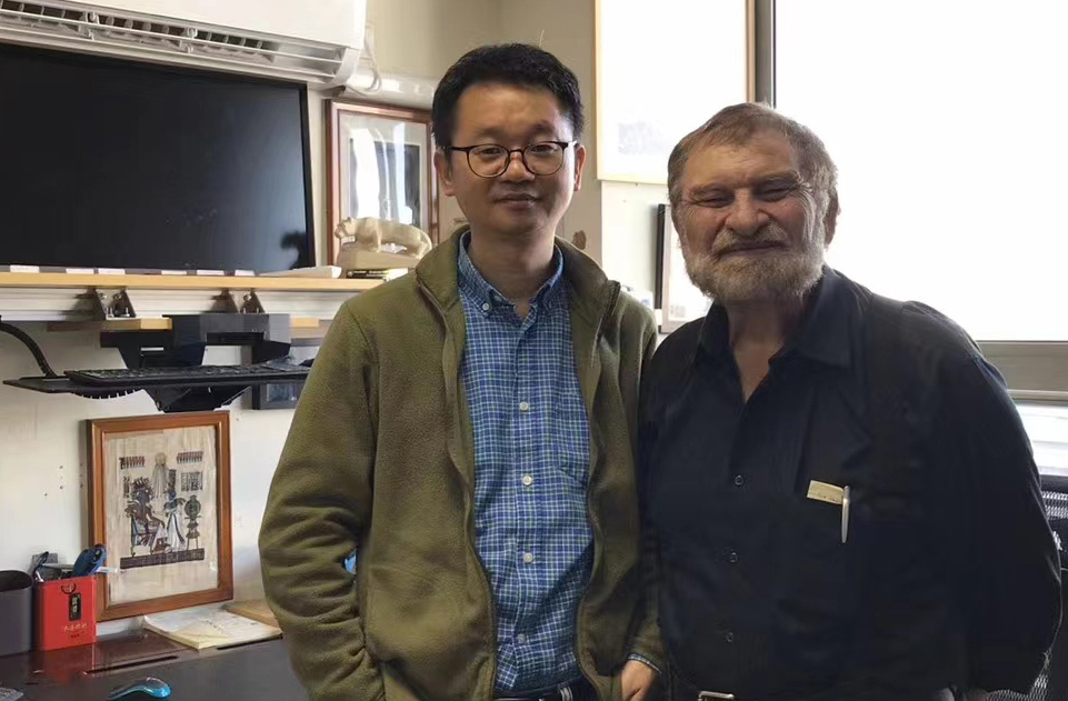 Two men stand together behind a desk in an office.