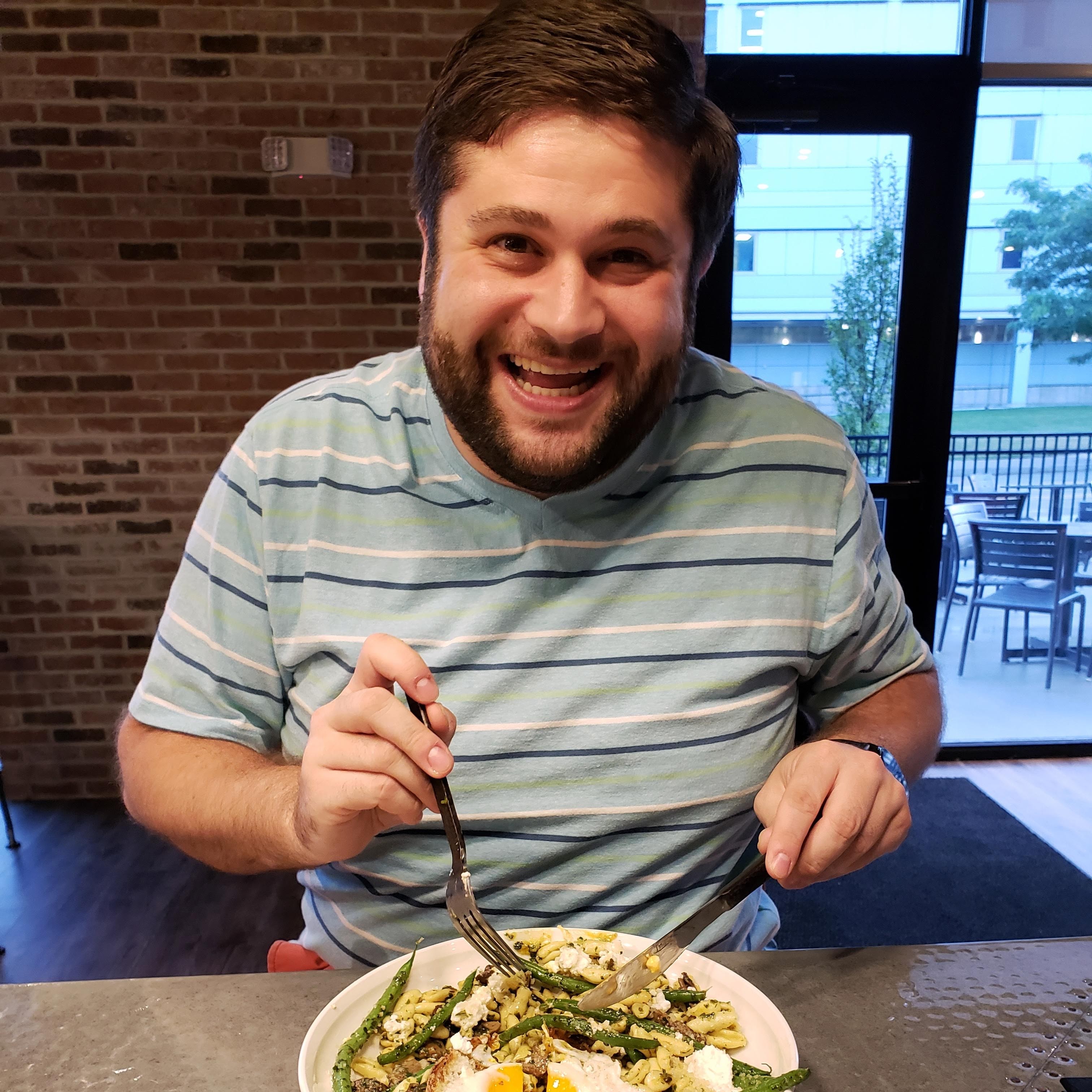 Alex Goodstein smiles for the camera while holding a fork and knife before taking his first bite of a meal