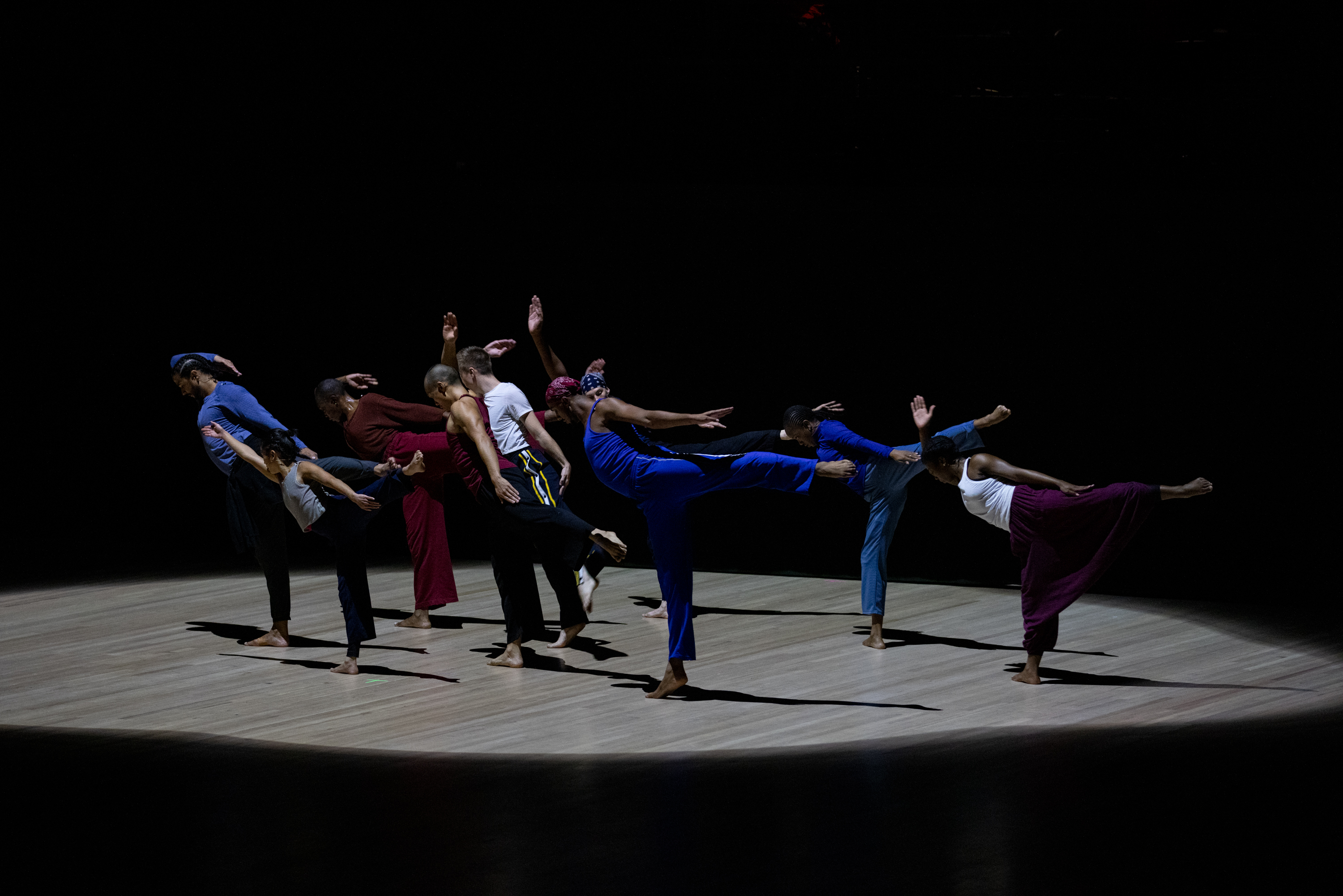 A small group pf dancers each stand on one leg and lean in the same direction.