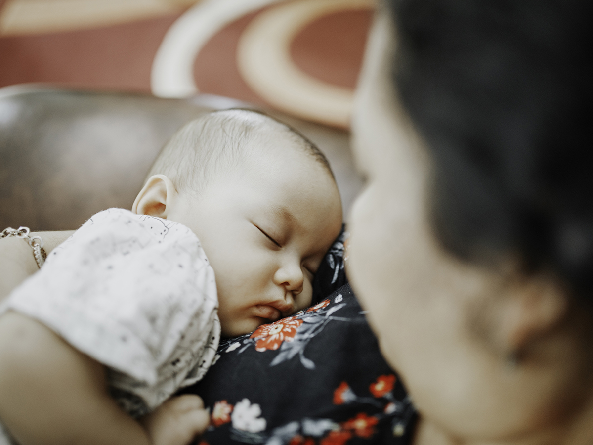 A woman looks down at her baby while holding them. 