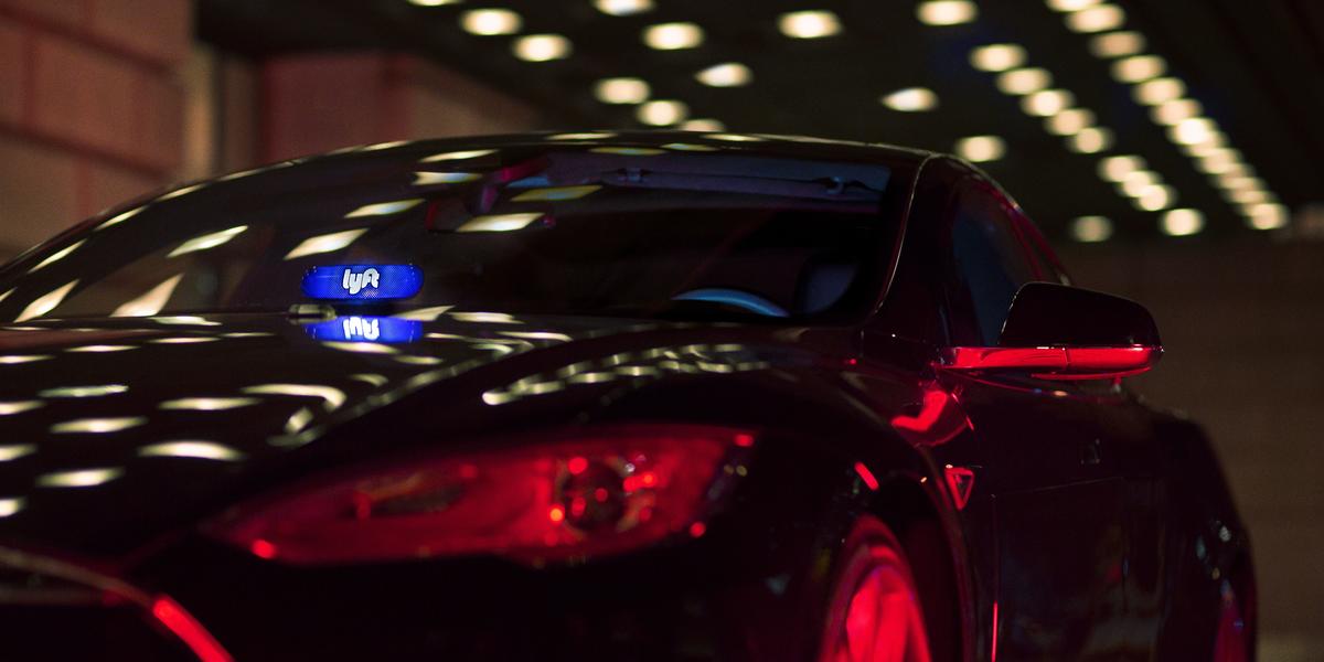 A black car driving at night with a Lyft sign illuminated in the front window