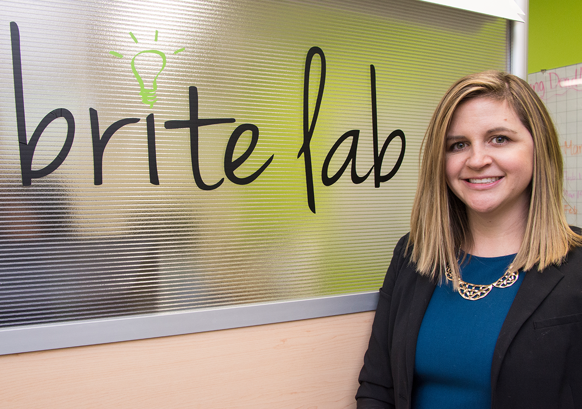 Person wearing a black blazer stands next to a sign that reads Brite Lab