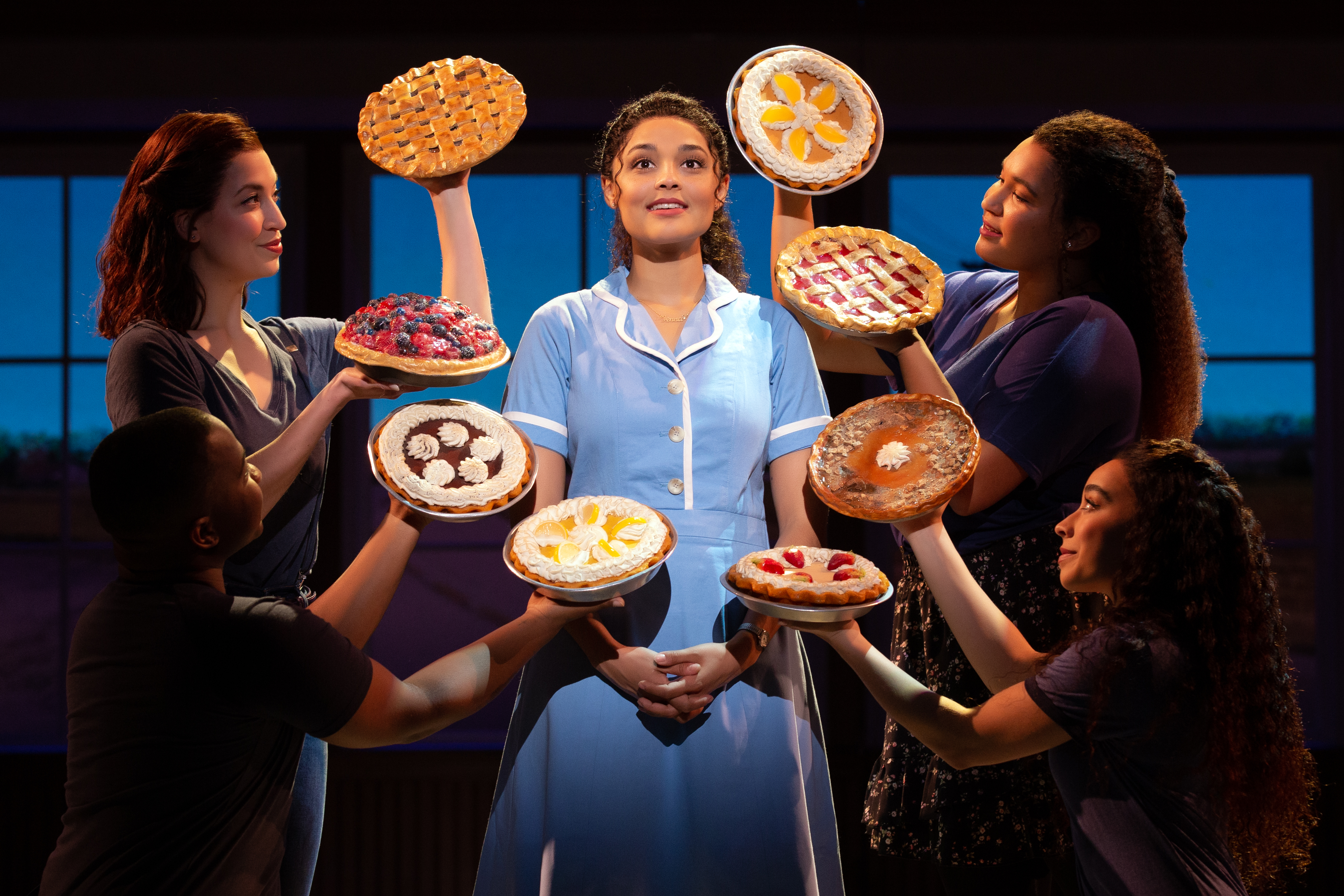 A woman stands surrounded by baked pies.