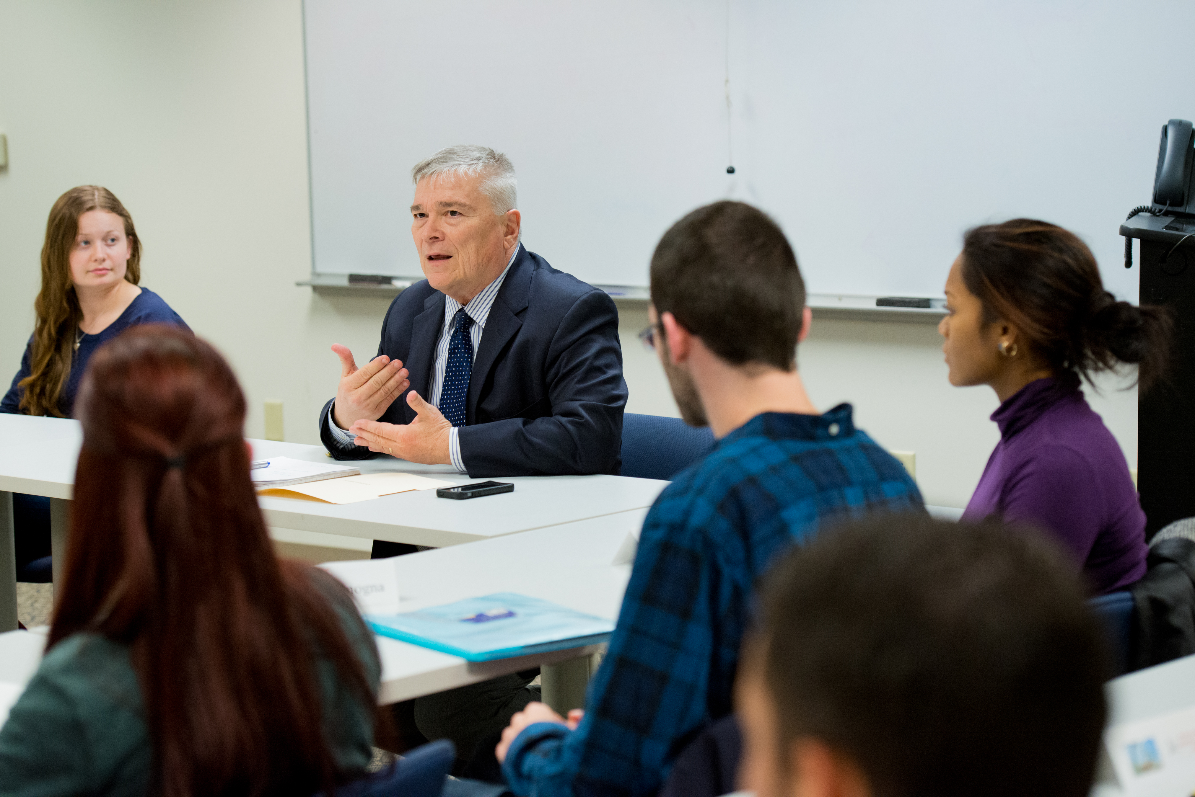 Penn State President Eric Barron sits alongside students at the front of a classroom, where he is speaking and teaching class.