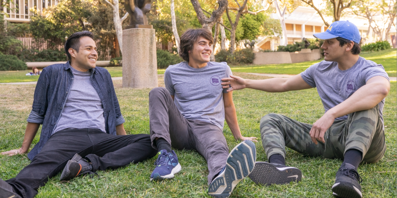 three fraternity members sitting in the grass