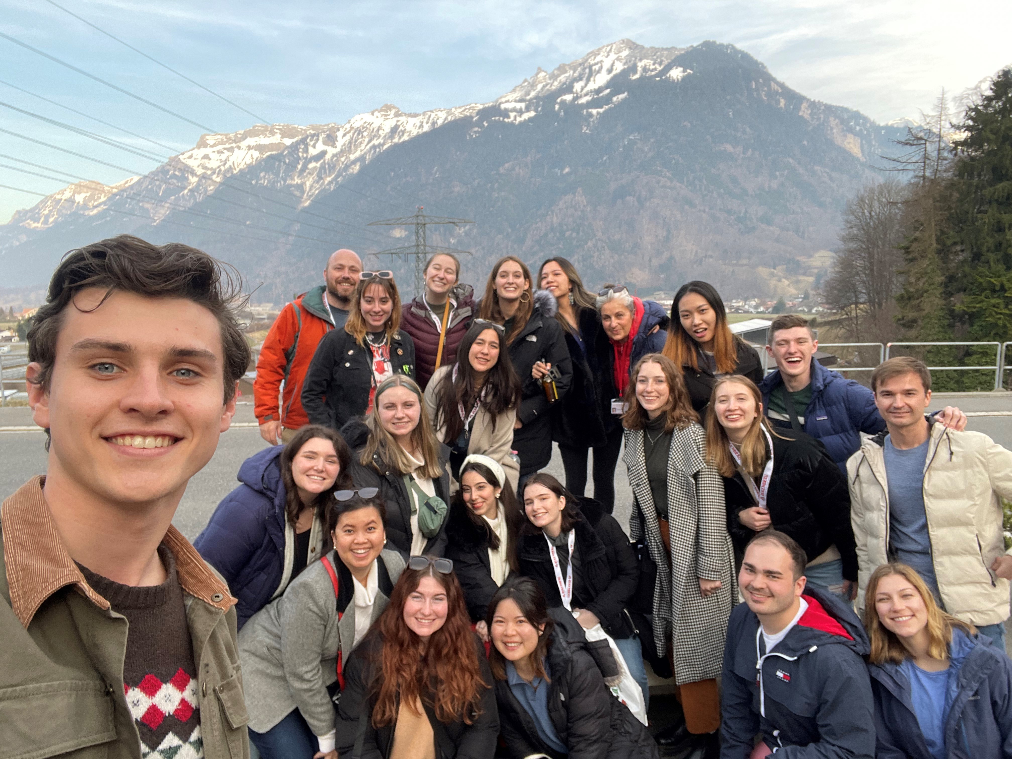 Students and faculty smiling at the camera in front of mountains in Switzerland