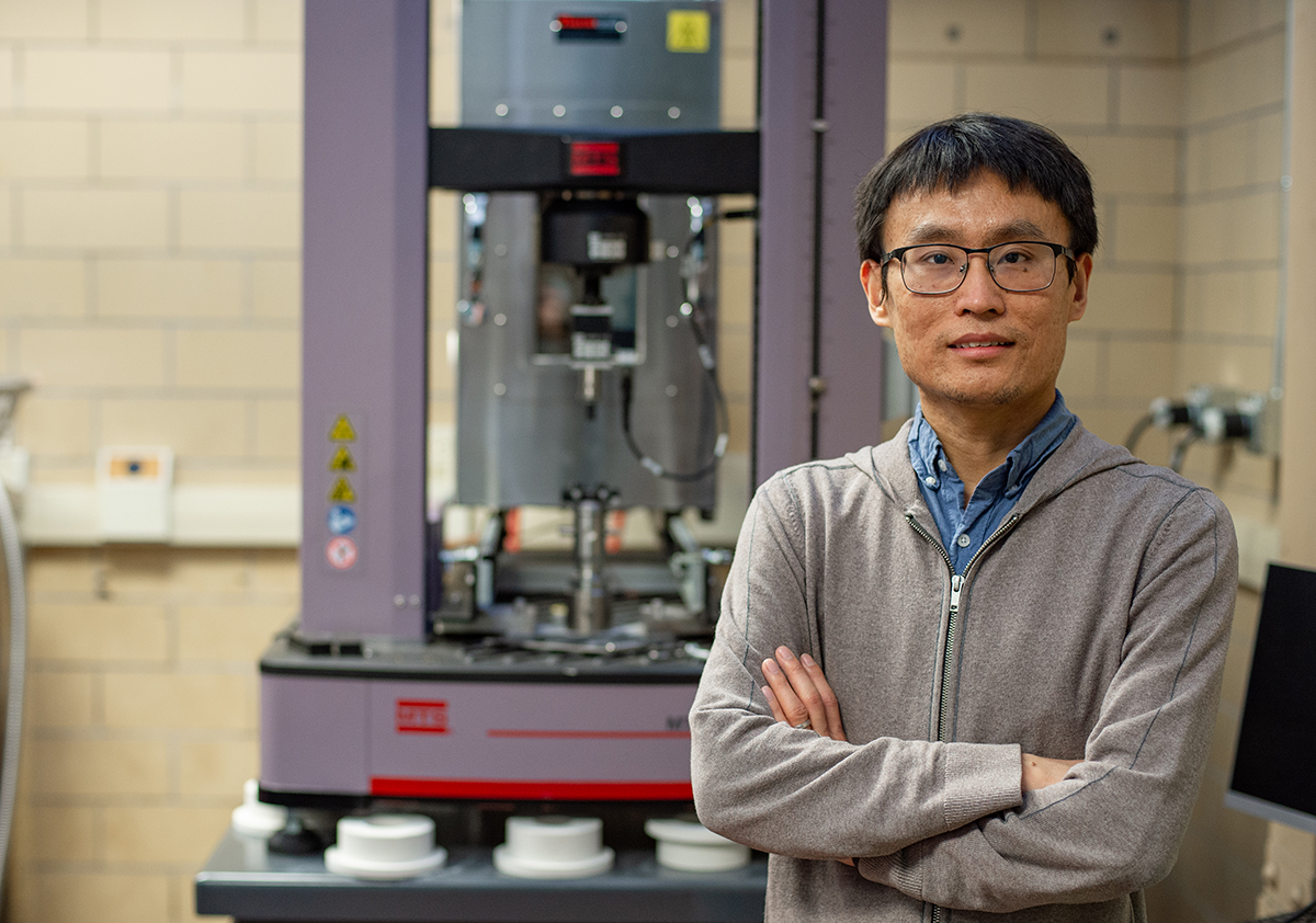 A man with arms crossed stands in front of a large piece of lab equipment. 