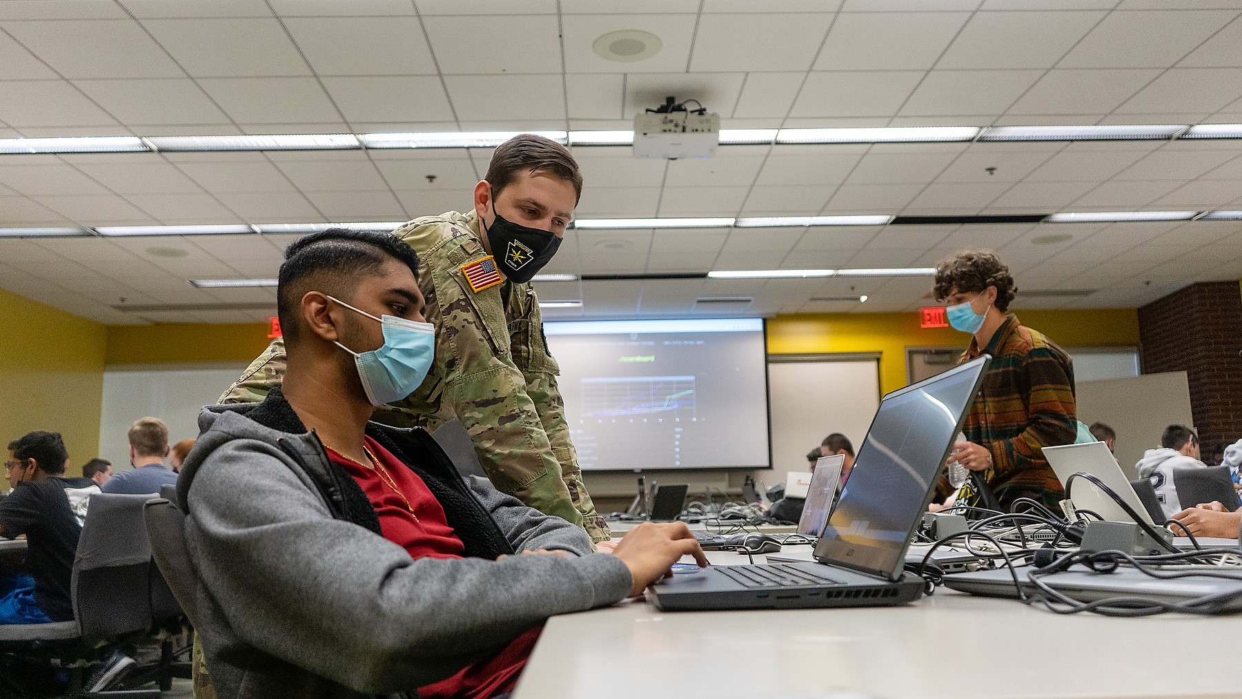 A PA National Guard member dressed in a a camoflauge uniform helps a student working on a laptop.