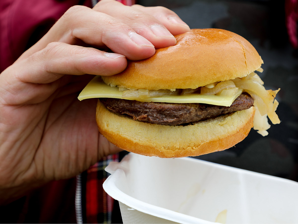 A hand holds a burger with onions and white cheese on it. 