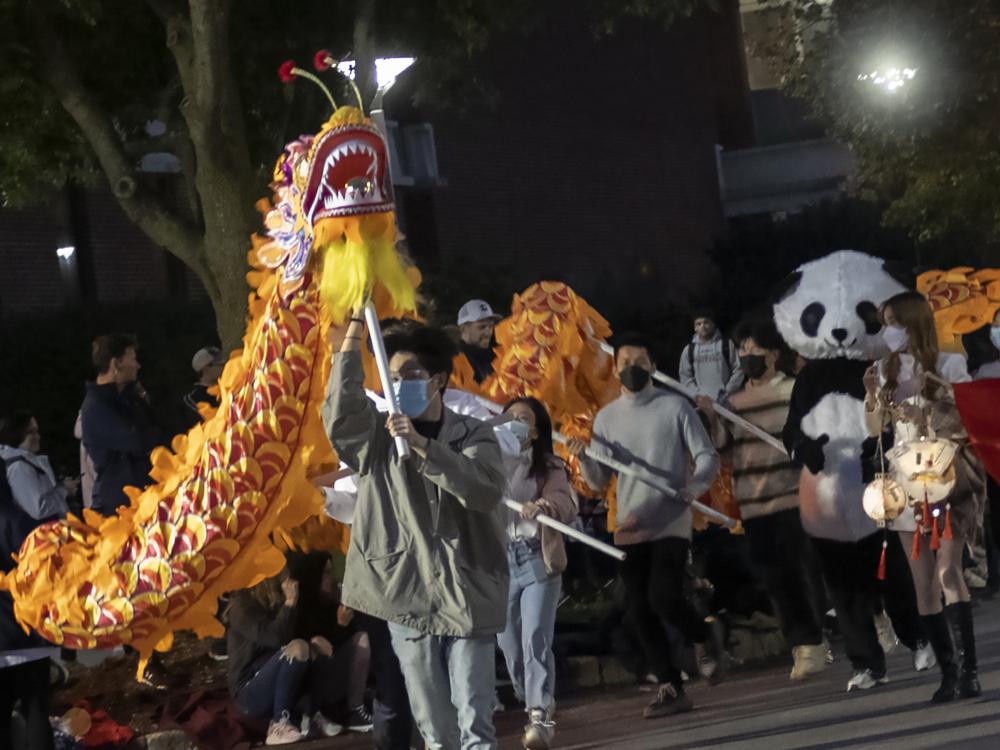 Several people manipulate a colorful yellow and orange dragon puppet down the street during a parade.