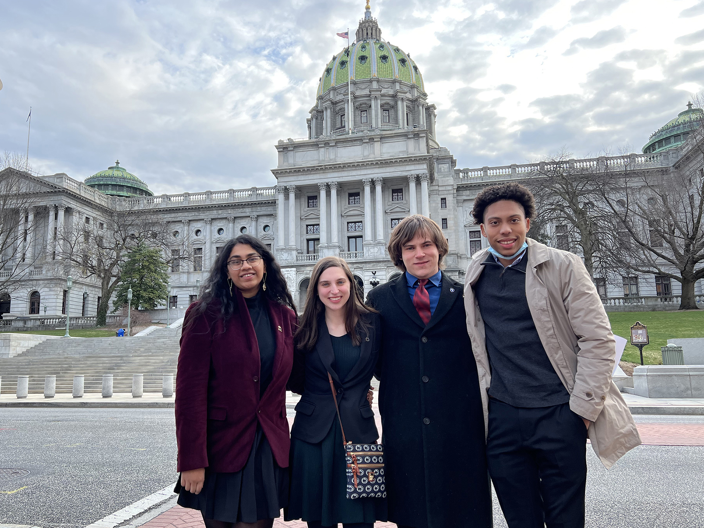 Four students stand in front of the Pennsylvania Capital Building