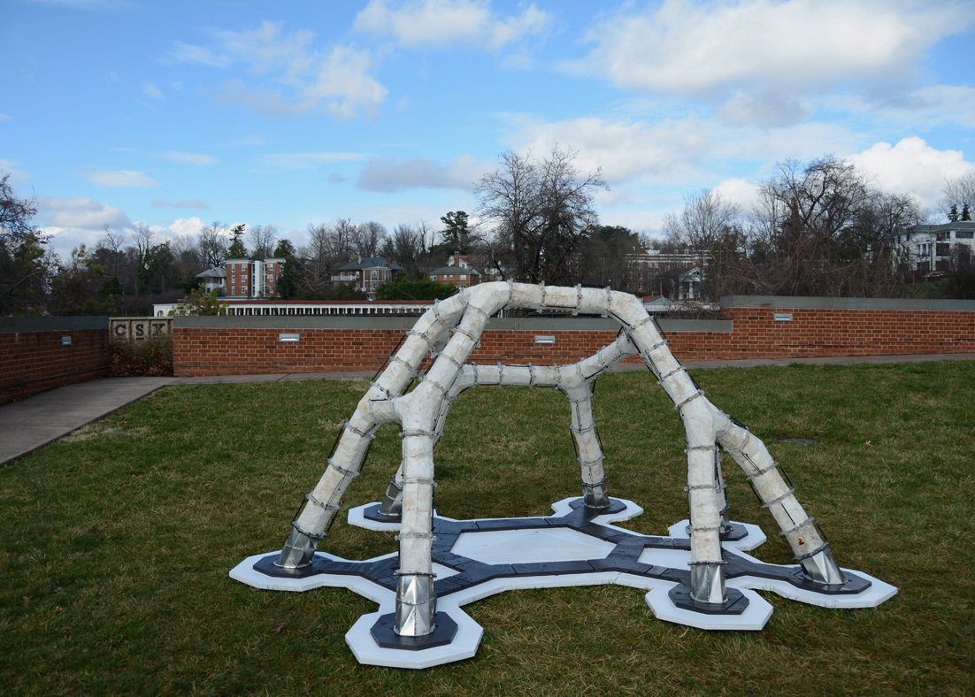 A white architectural structure with six legs on a patch of grass. 