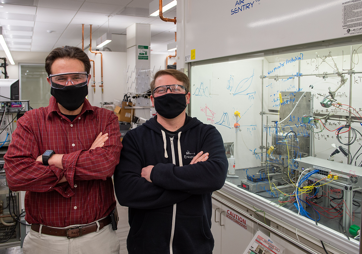 Two men with arms crossed stand in a lab.