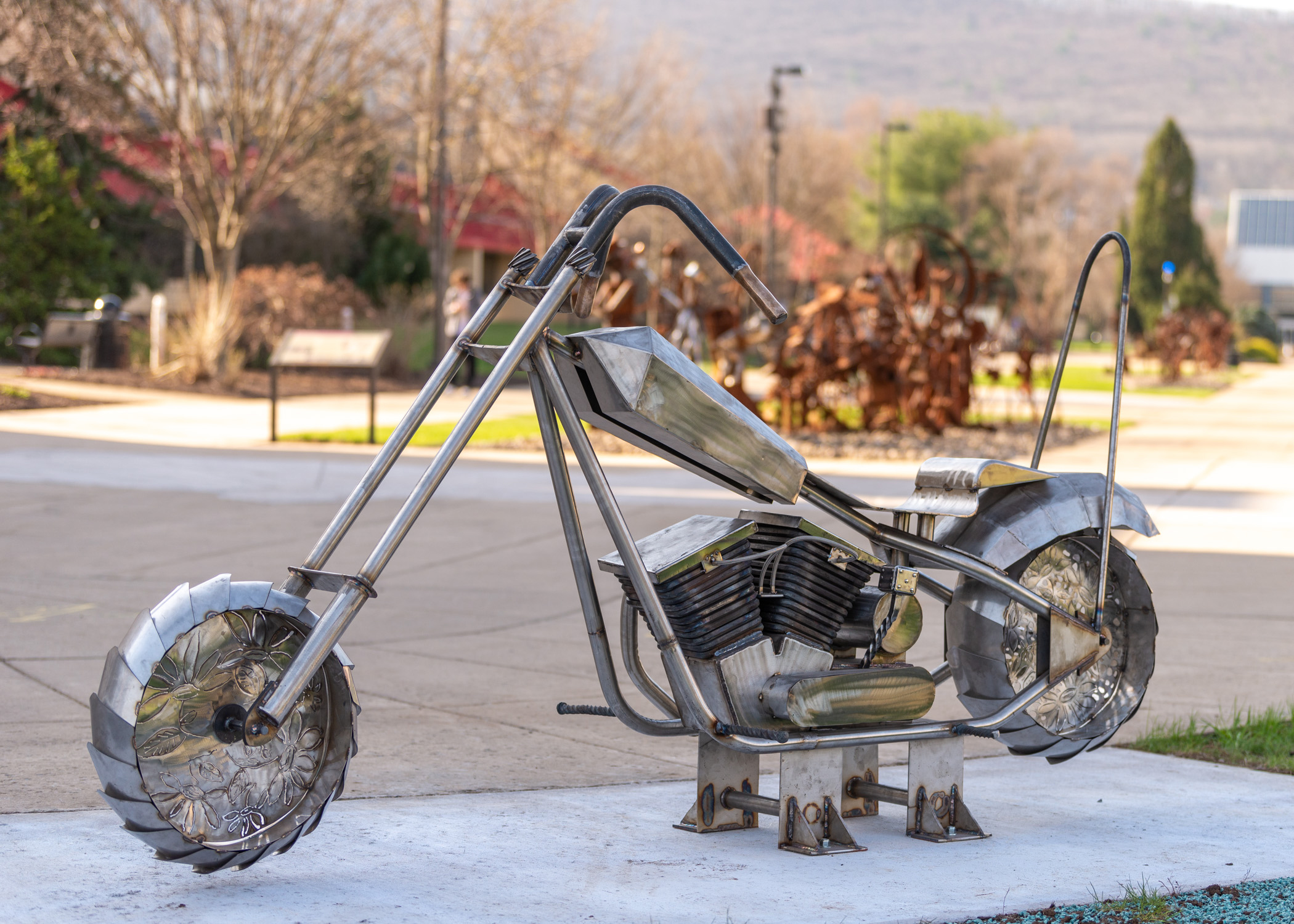 A sculpture of a stainless steel motorcycle outside on a platform