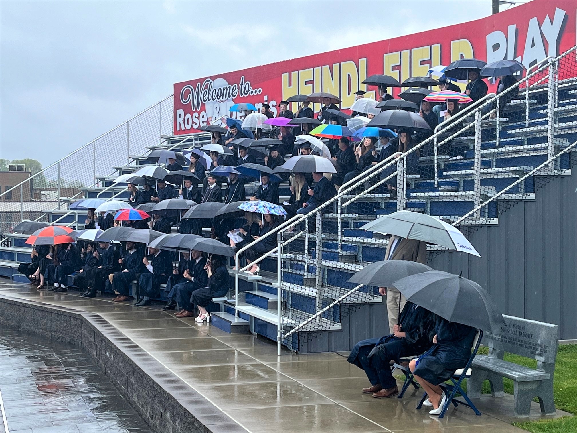 graduating students in bleachers with umbrellas