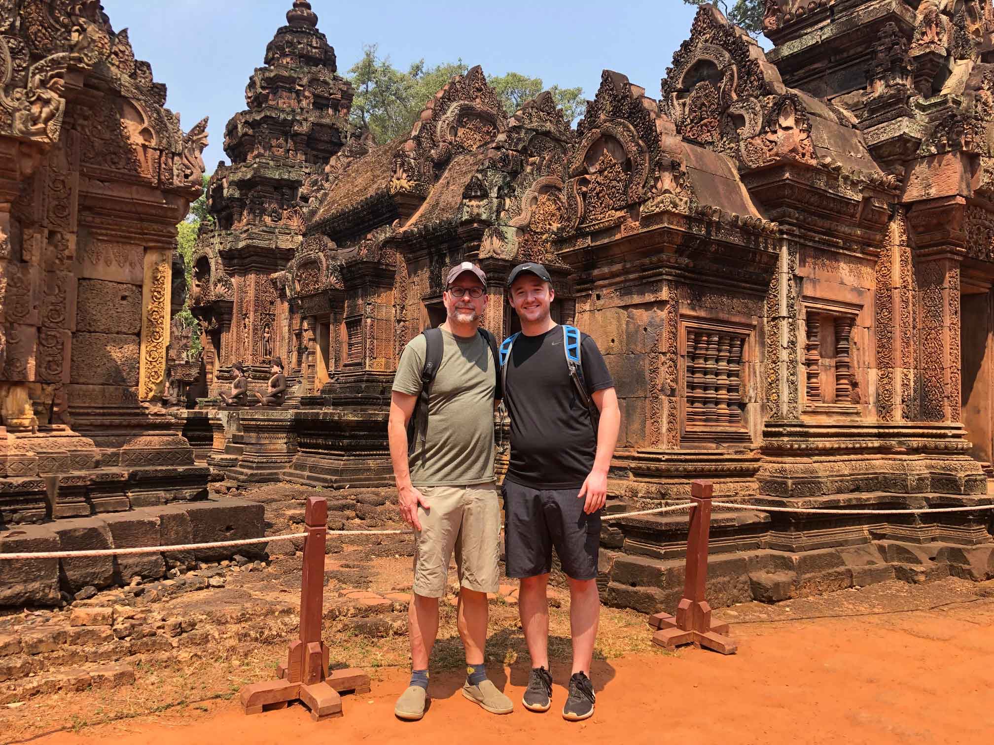 two men standing in front of statues in Angkor Wat, Cambodia