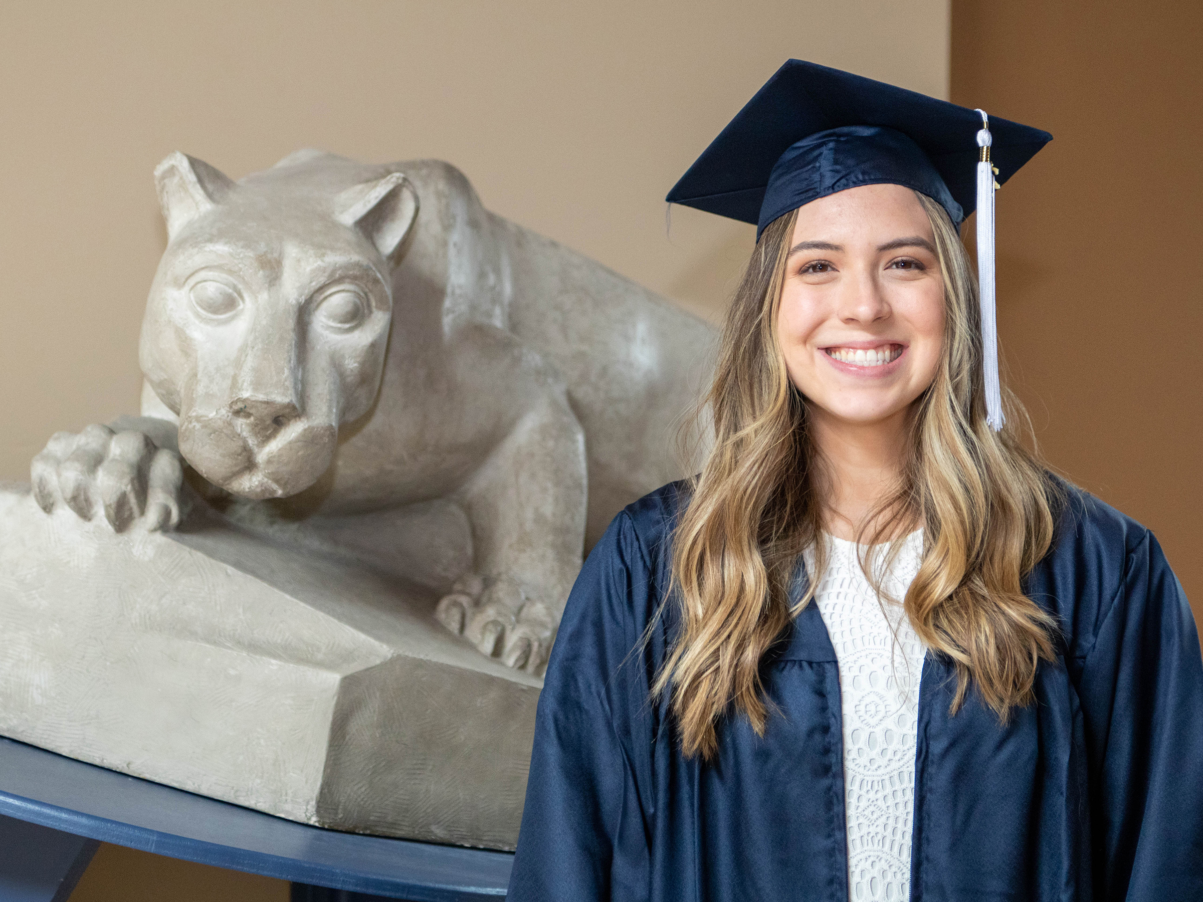 Rachel Maynard in cap and gown next to small Nittany Lion Shrine. 