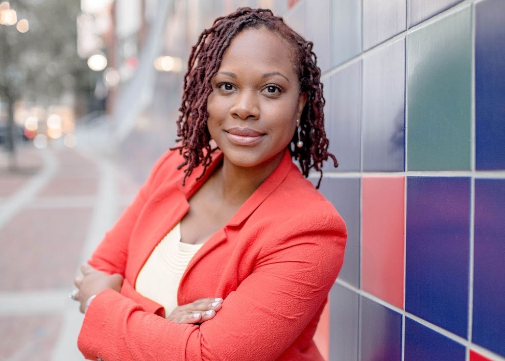 Portrait of Timeka Tounsel wearing an orange blazer with her arms crossed across her chest