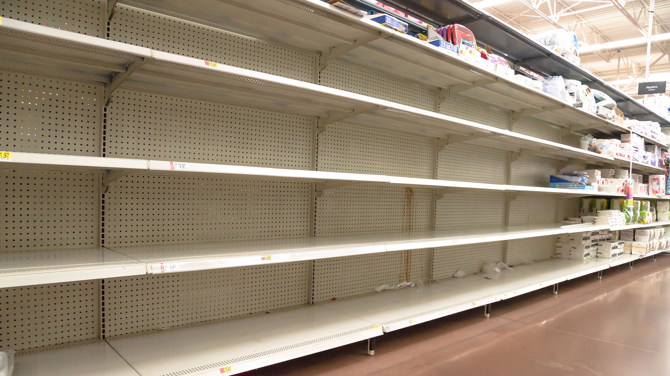 Four empty shelves at a grocery store are shown