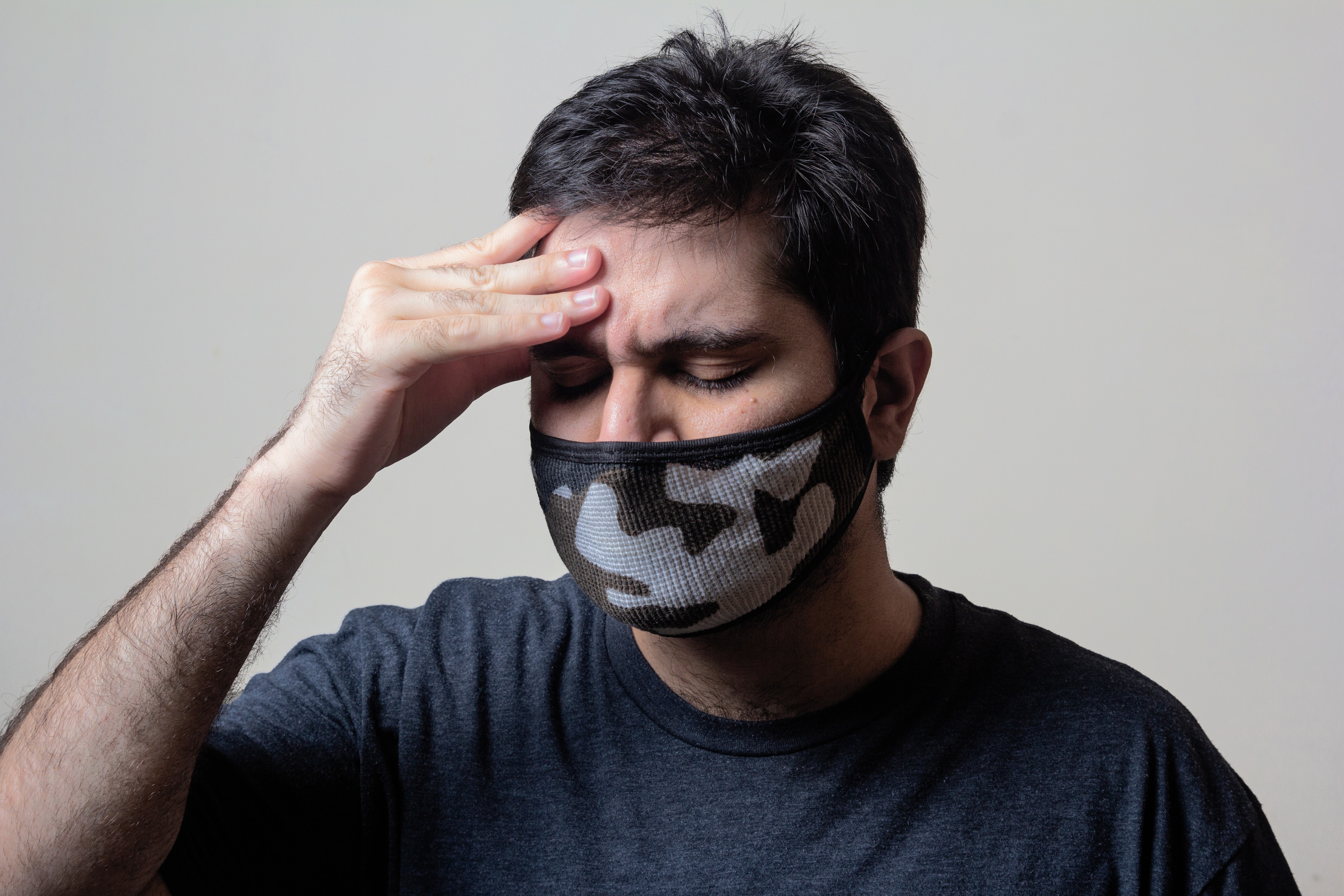 Man wearing a medical face mask wincing and gripping his forehead