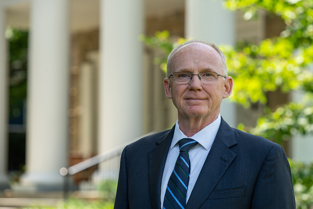 Anthony Atchley stands outdoors with greenery and building in background.