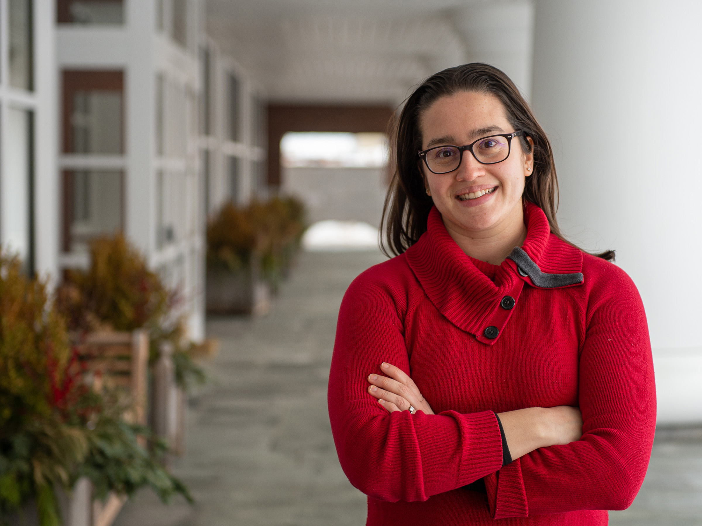 An individual wearing a red sweater with arms crossed poses outdoors. 