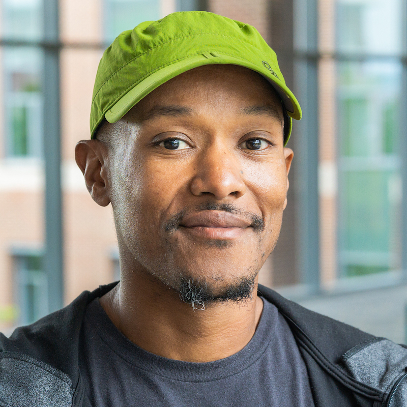 A man looks at the camera wear a green ball cap 