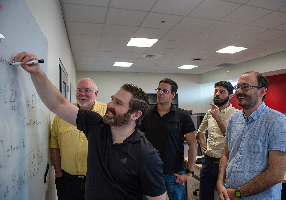 Five researchers gaze at a whiteboard in a classroom. 