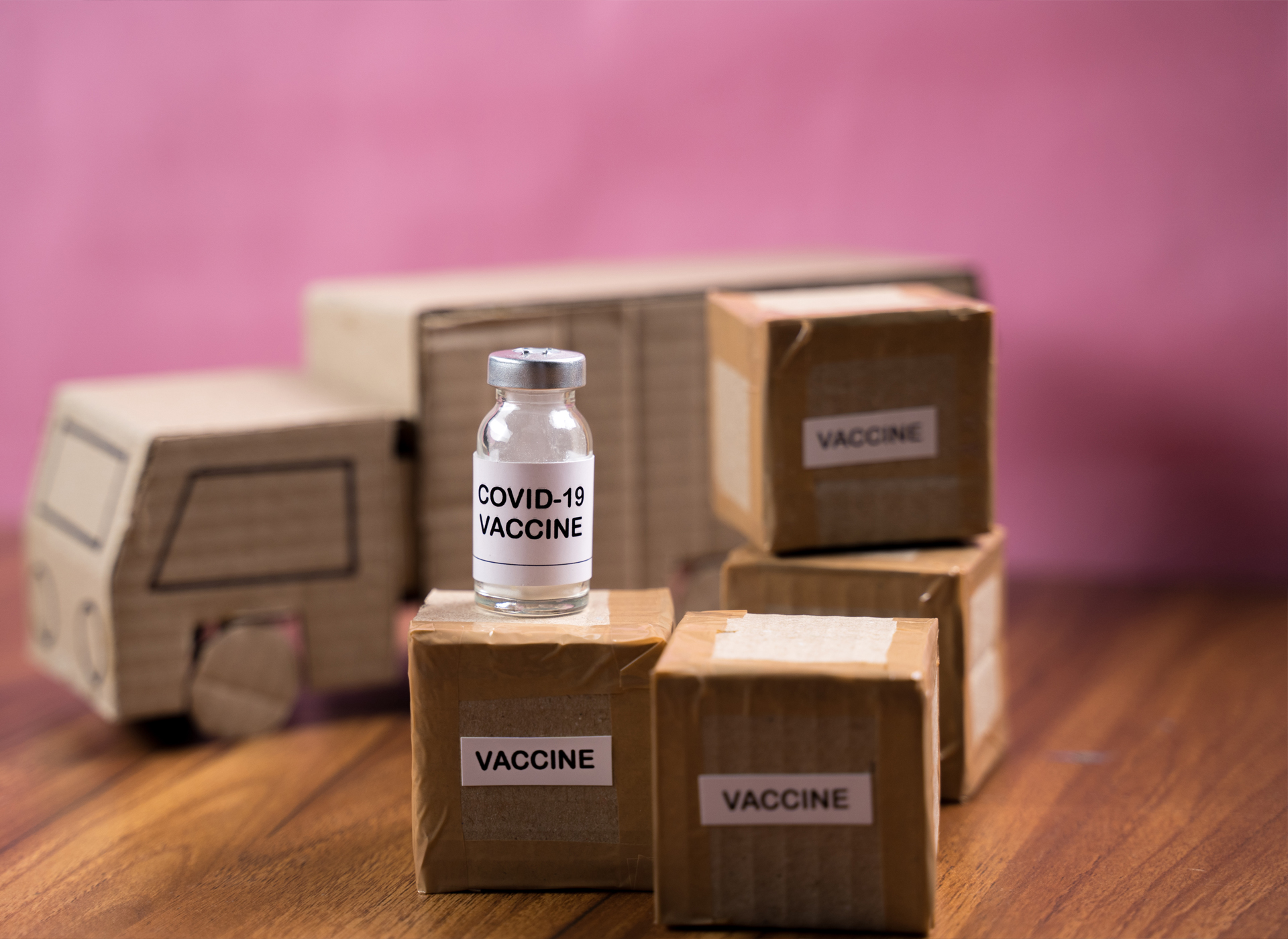 A cardboard truck and small cardboard boxes represent distribution of COVID-19 vaccinations