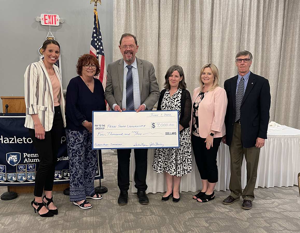 Six individuals standing in a row holding large check.