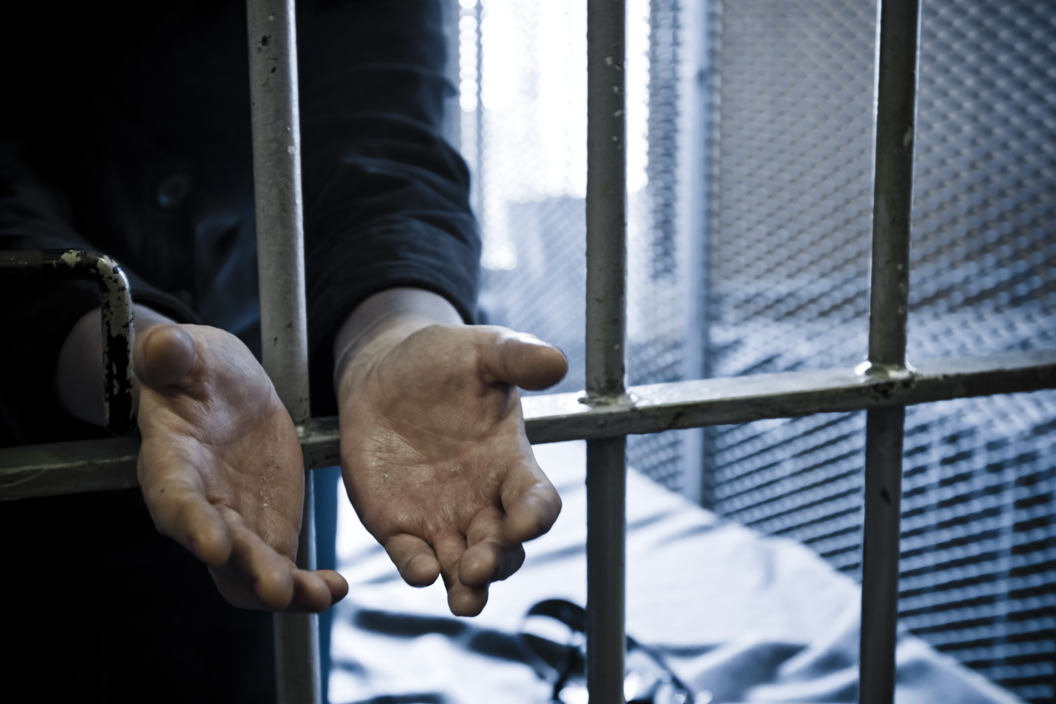 Handcuffed hands reaching out through a barred cell door