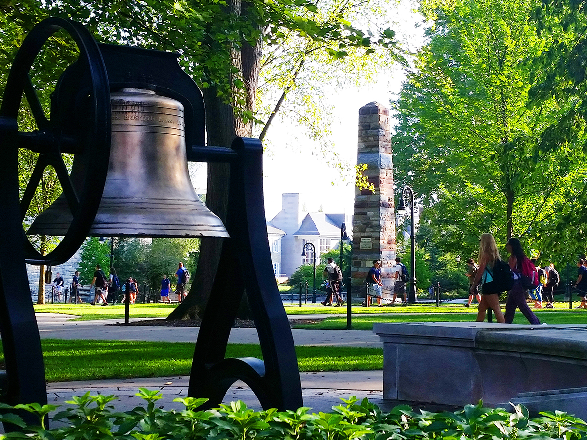 The Old Main bell at University Park with students walking in the background.