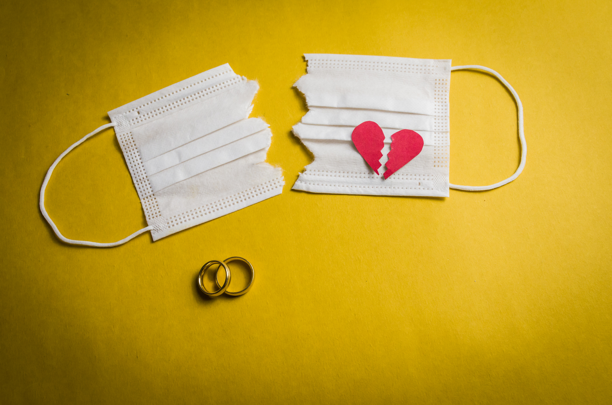 A white medical face mask cut in half with a broken heart on one side