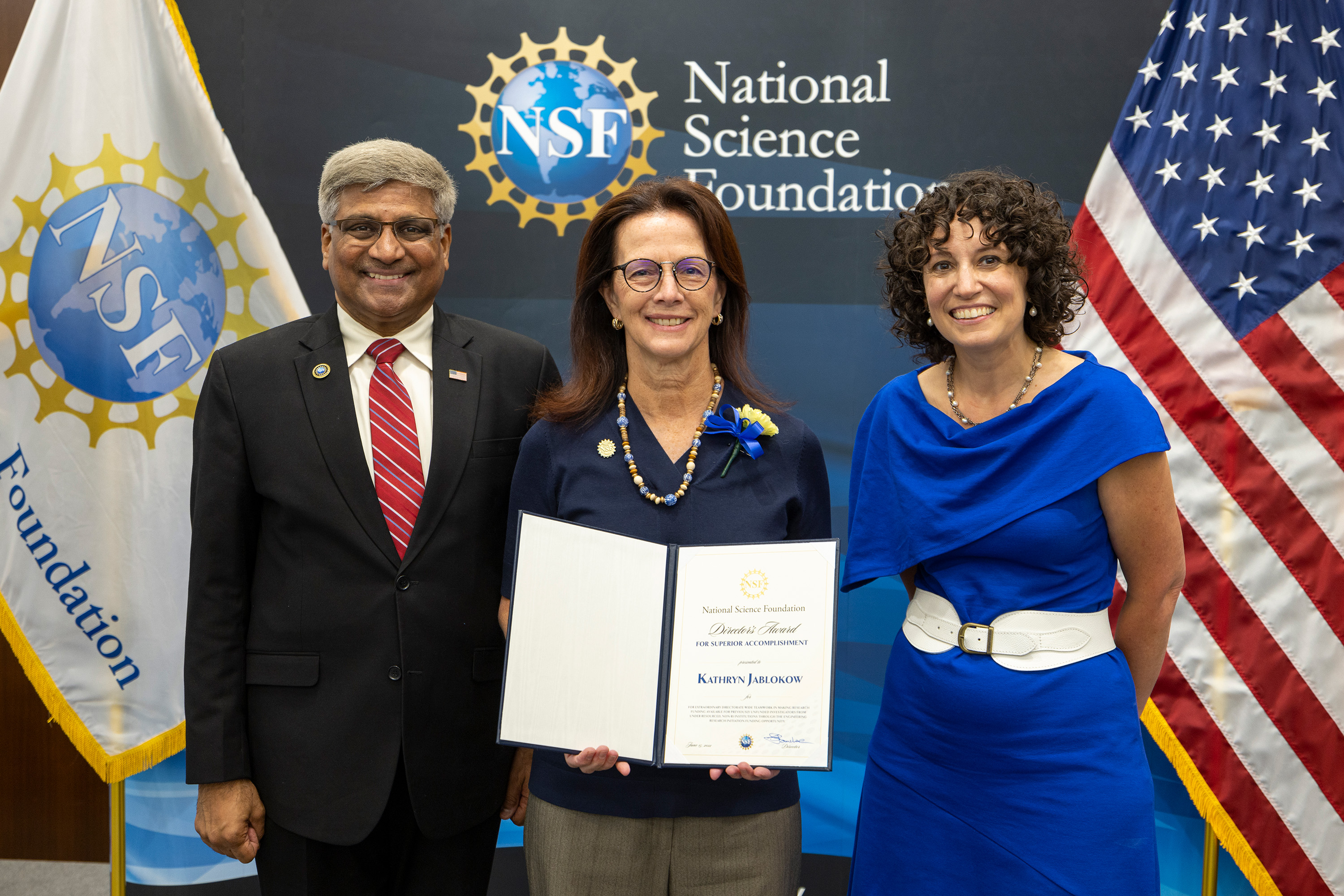 Three people standing in front of a wall with the NSF logo. Kathryn Jablokow is in the middle, holding an award.