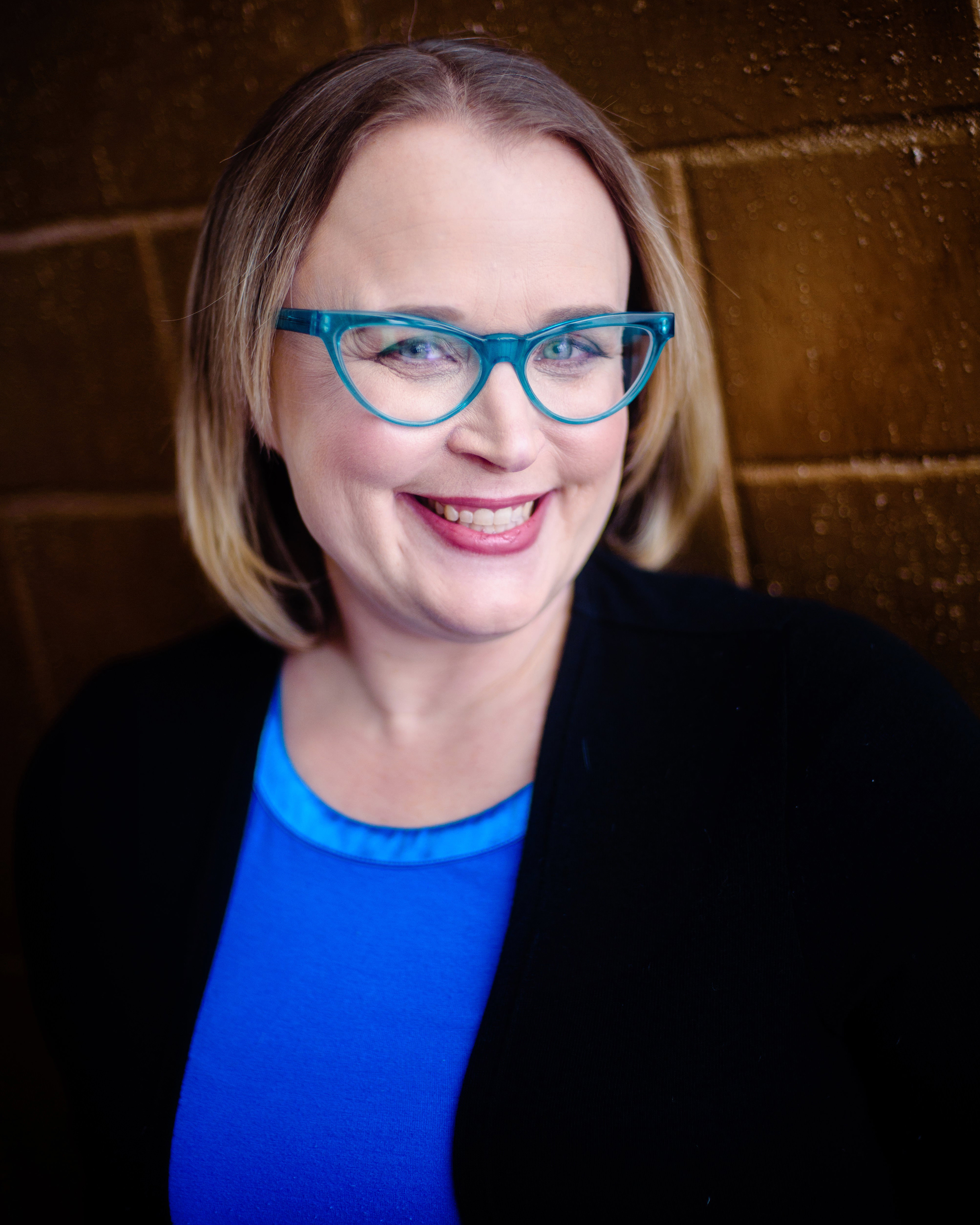 Portrait of woman wearing eyeglasses, a blue blouse and a black jacket.