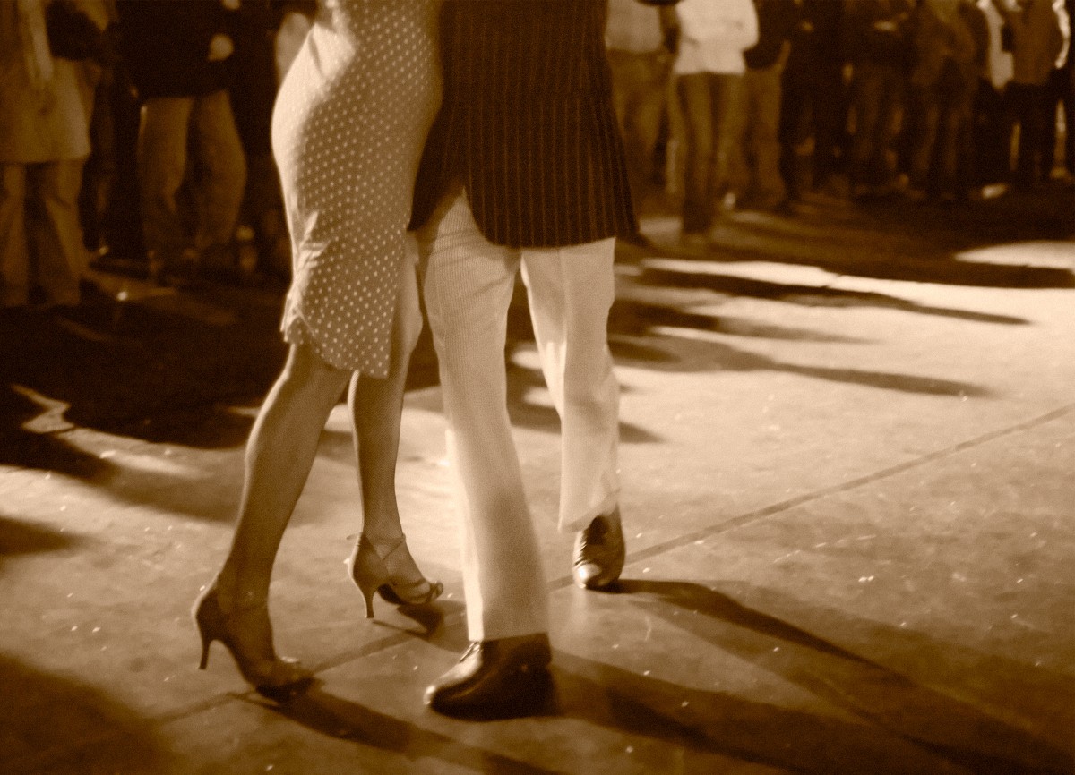 A man and woman dance the Argentine Tango outdoors while a crowd watches.