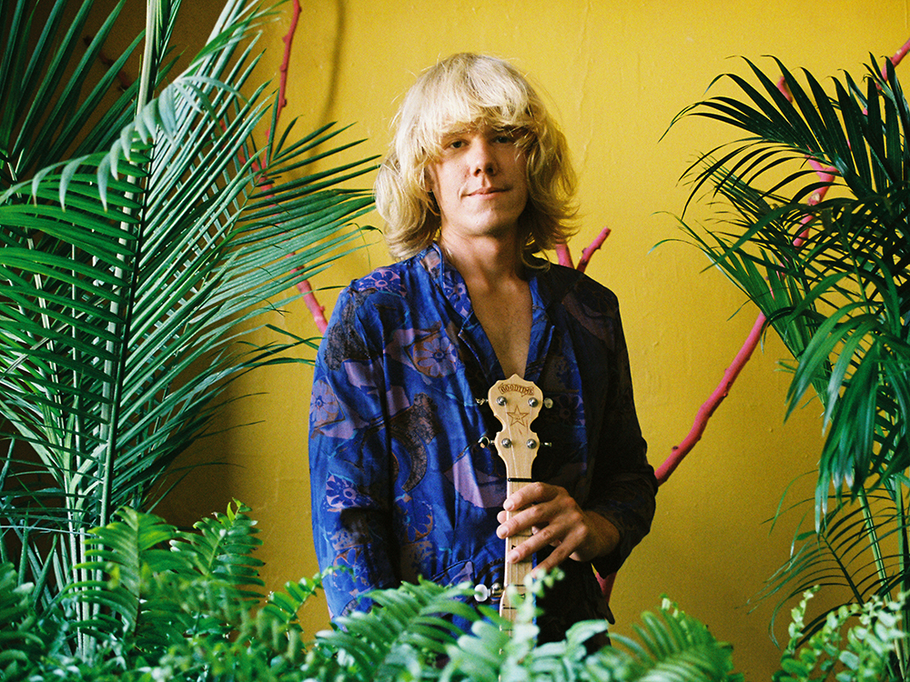 Jay Johnson holds a bouzouki behind and next to plants