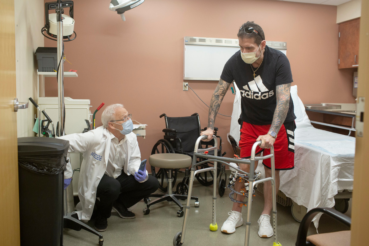 A doctor works with a patient that has a walker, and you can see an external device on the patient's leg that is used to correct bone deformities 