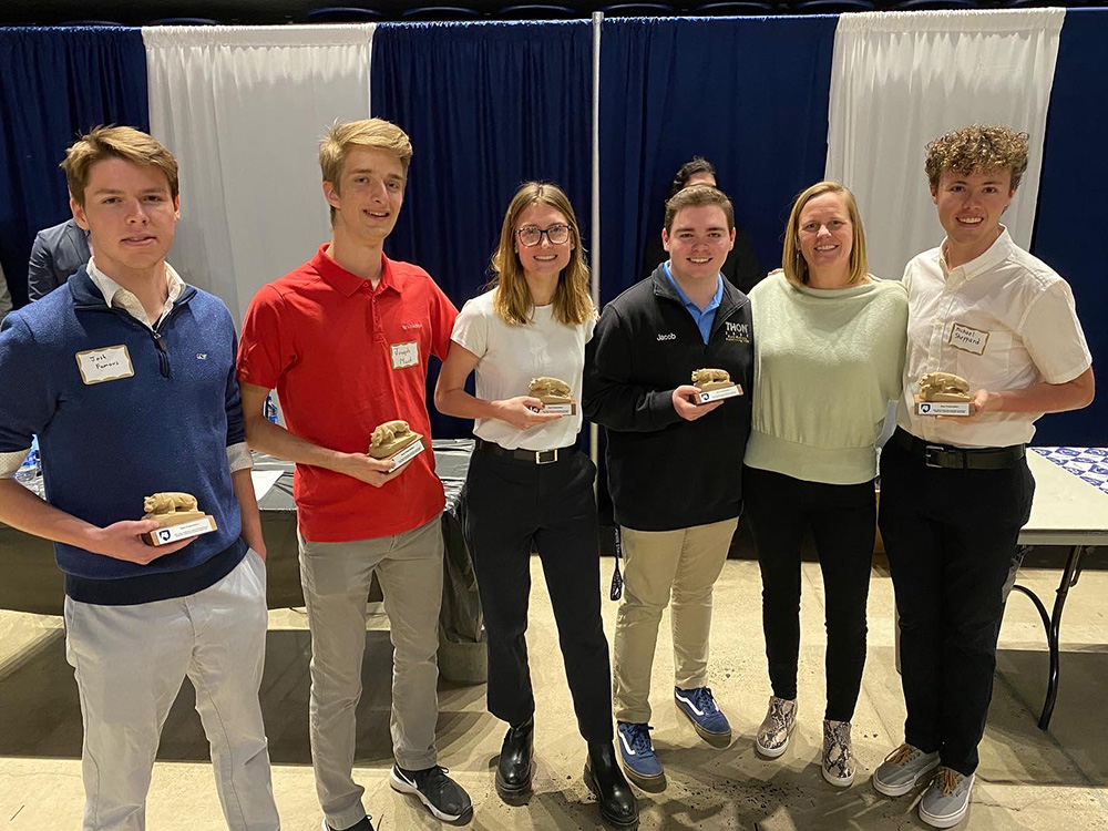 A group of students smile and pose while holding small statues of the Nittany Lion. 