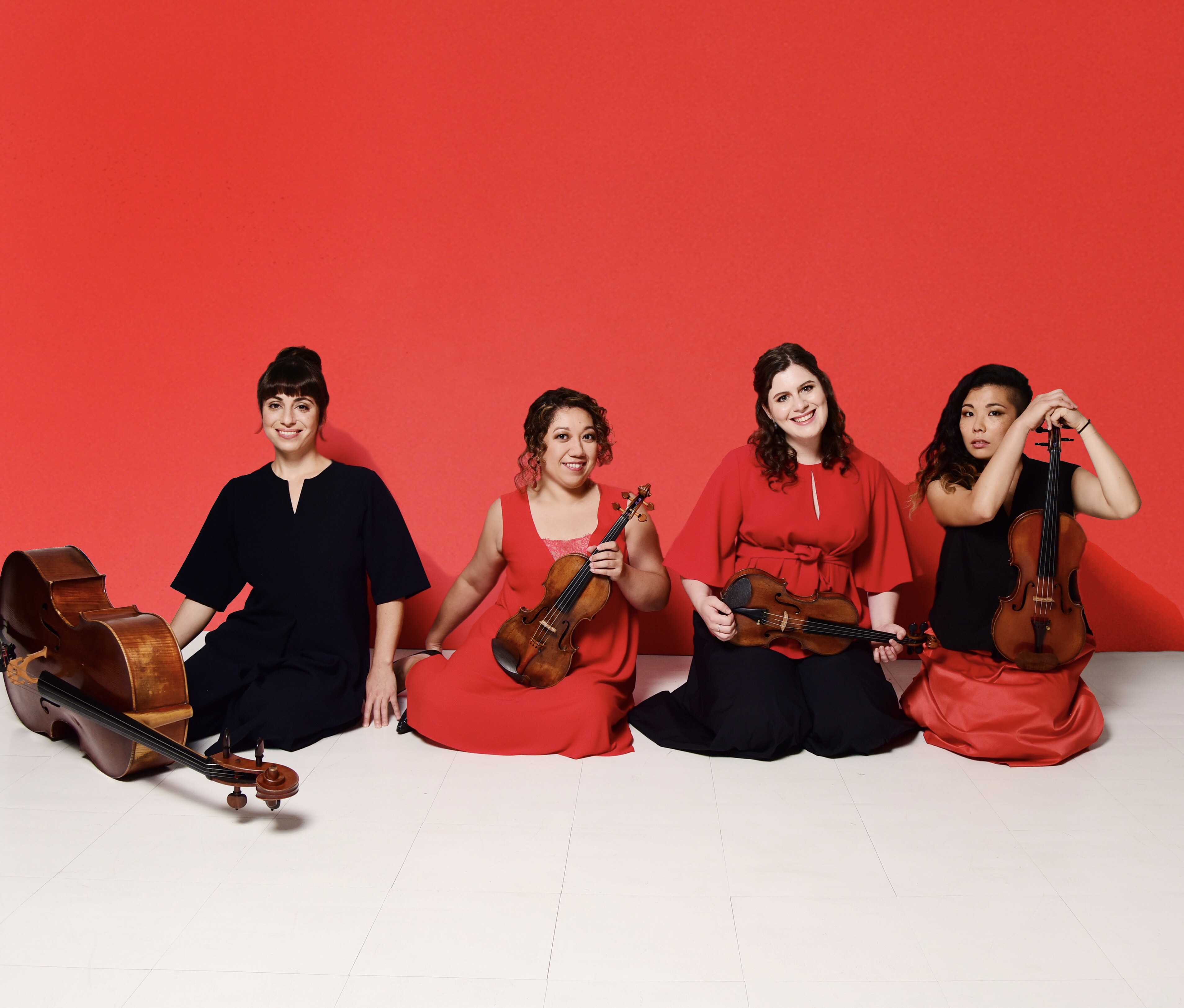 Four woman musicians sit in a row and hold their stringed instruments.