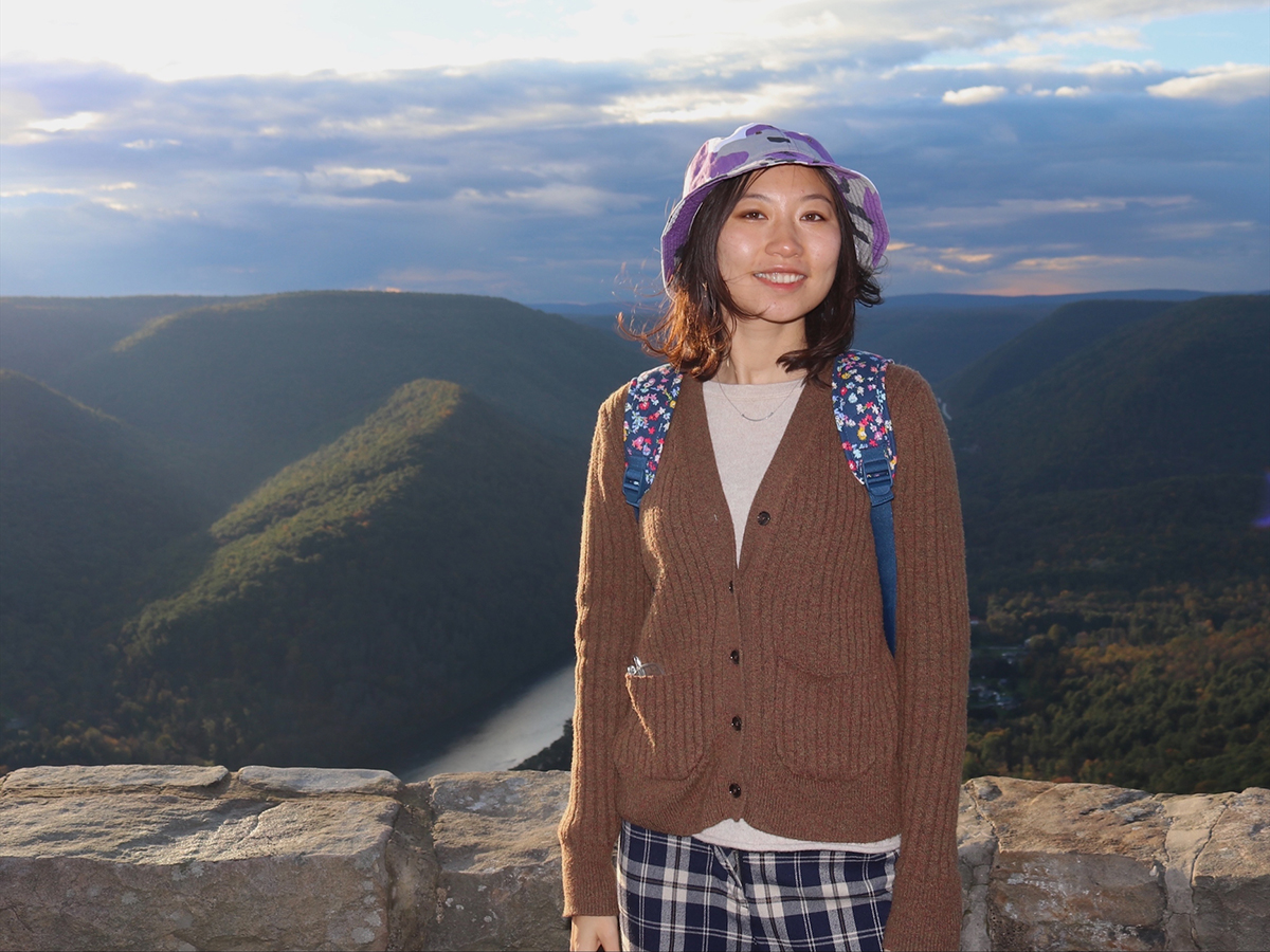 Shuyu Chang, pictured before a stone wall, with forested mountains and a river in the background