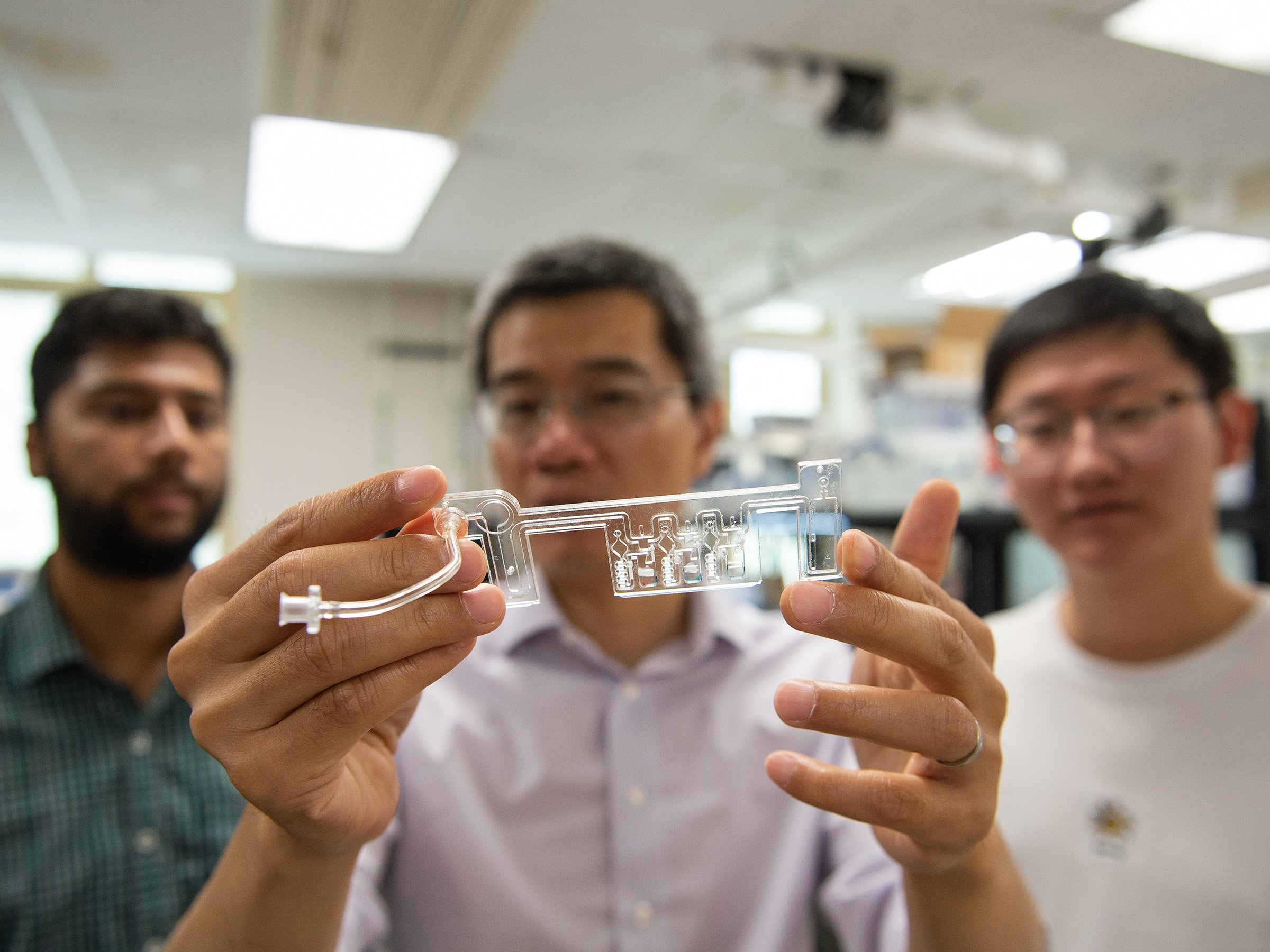 Three individuals display a COVID-19 test kit in a lab.